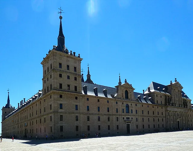 The west side of El Escorial, with a tall corner tower and slate roofs against a blue sky