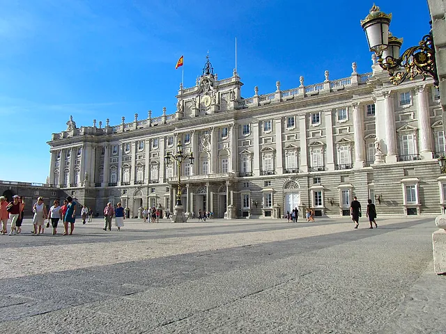 The Royal Palace of Madrid on a sunny day, seen from the Plaza de la Armería with visitors in front
