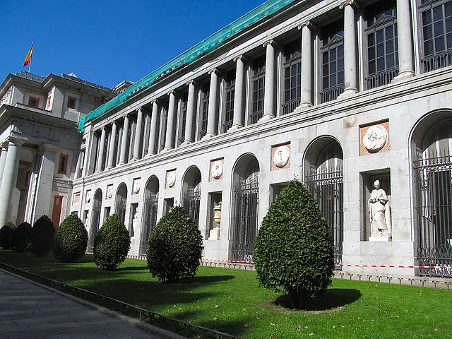 A long colonnaded wing of the Prado Museum with clipped bushes in front